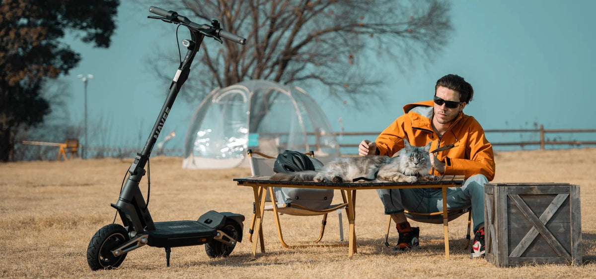 Electric scooter parked by an outdoor picnic table where a man sits – how much does an electric scooter weigh to take along