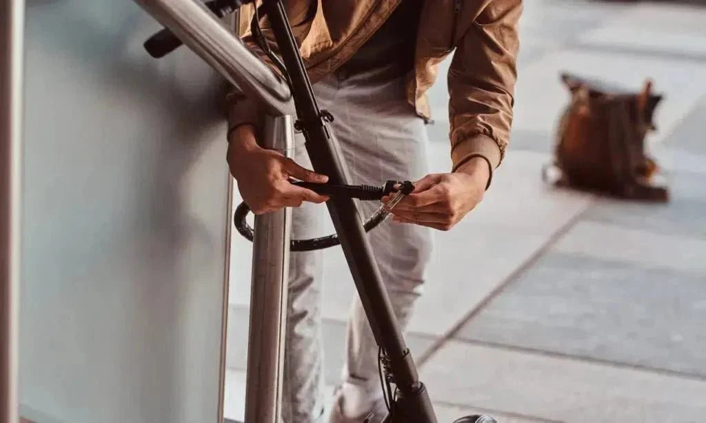 Person locking an electric scooter to a railing with a thin cable lock – how to protect it from theft