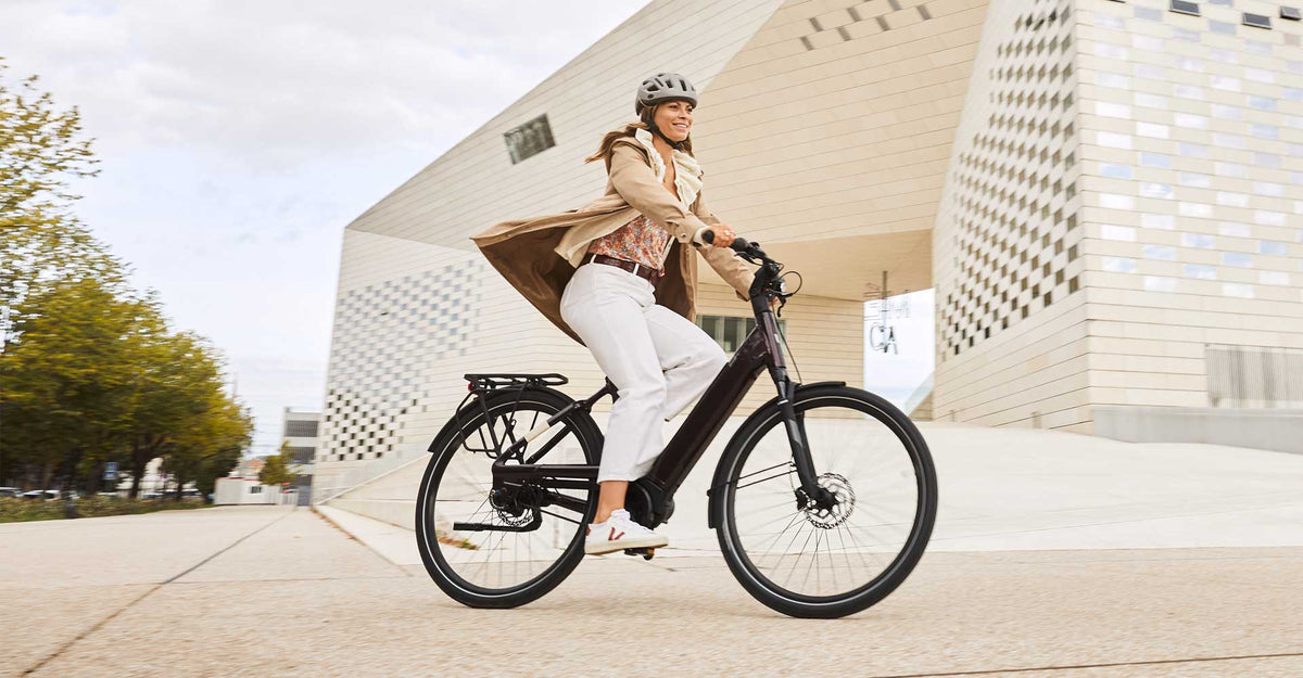 Woman in a helmet riding an e-bike past a modern building – electric bike laws in Europe