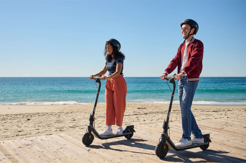 Two people in helmets riding electric scooters on a beachside boardwalk – could one replace the car on your commute?