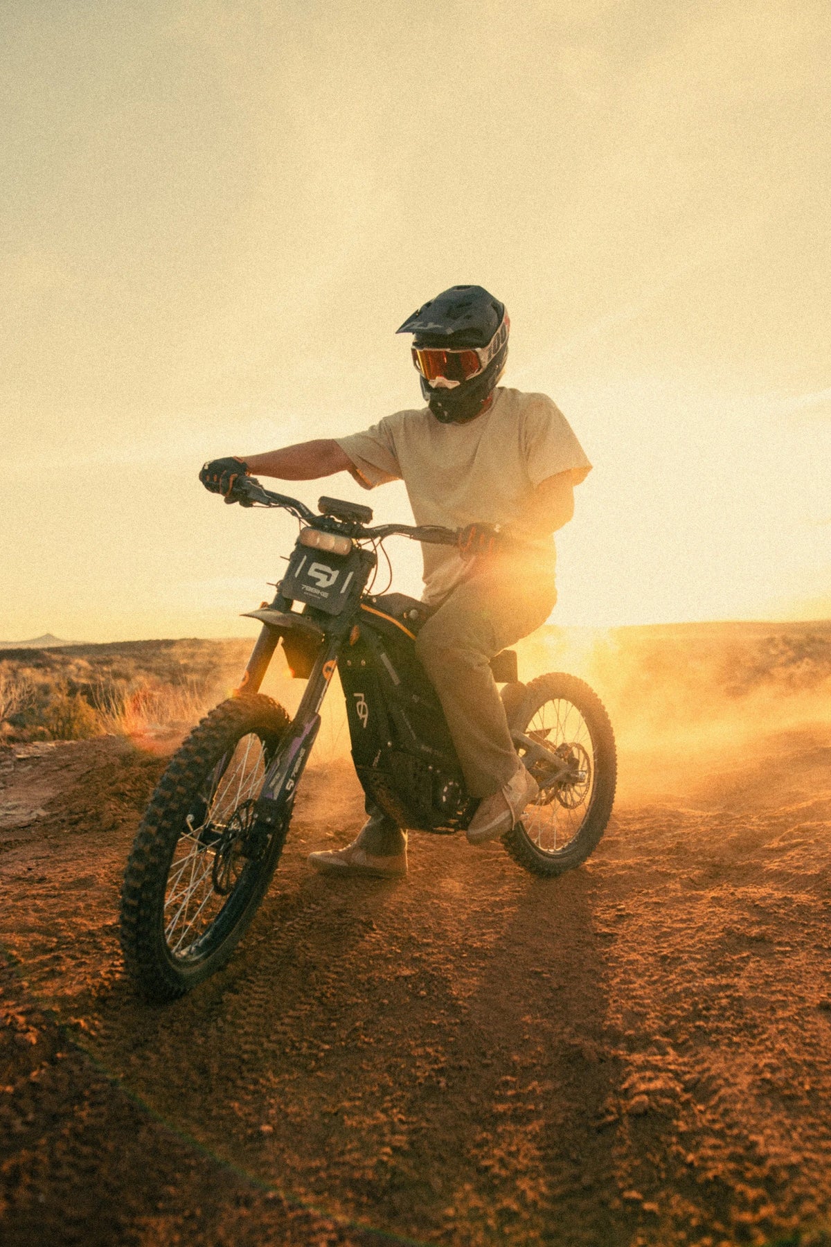 Person riding the 79BIKE Falcon Pro electric dirt bike on sandy ground at sunset
