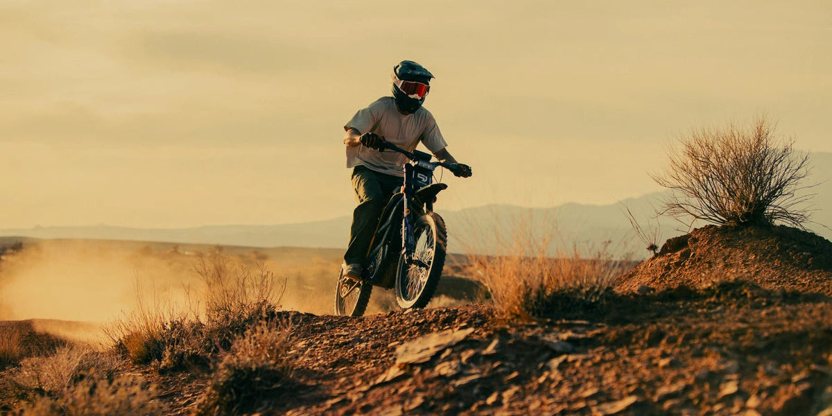 Person riding the 79BIKE Falcon Pro electric dirt bike on a grassy field at sunset