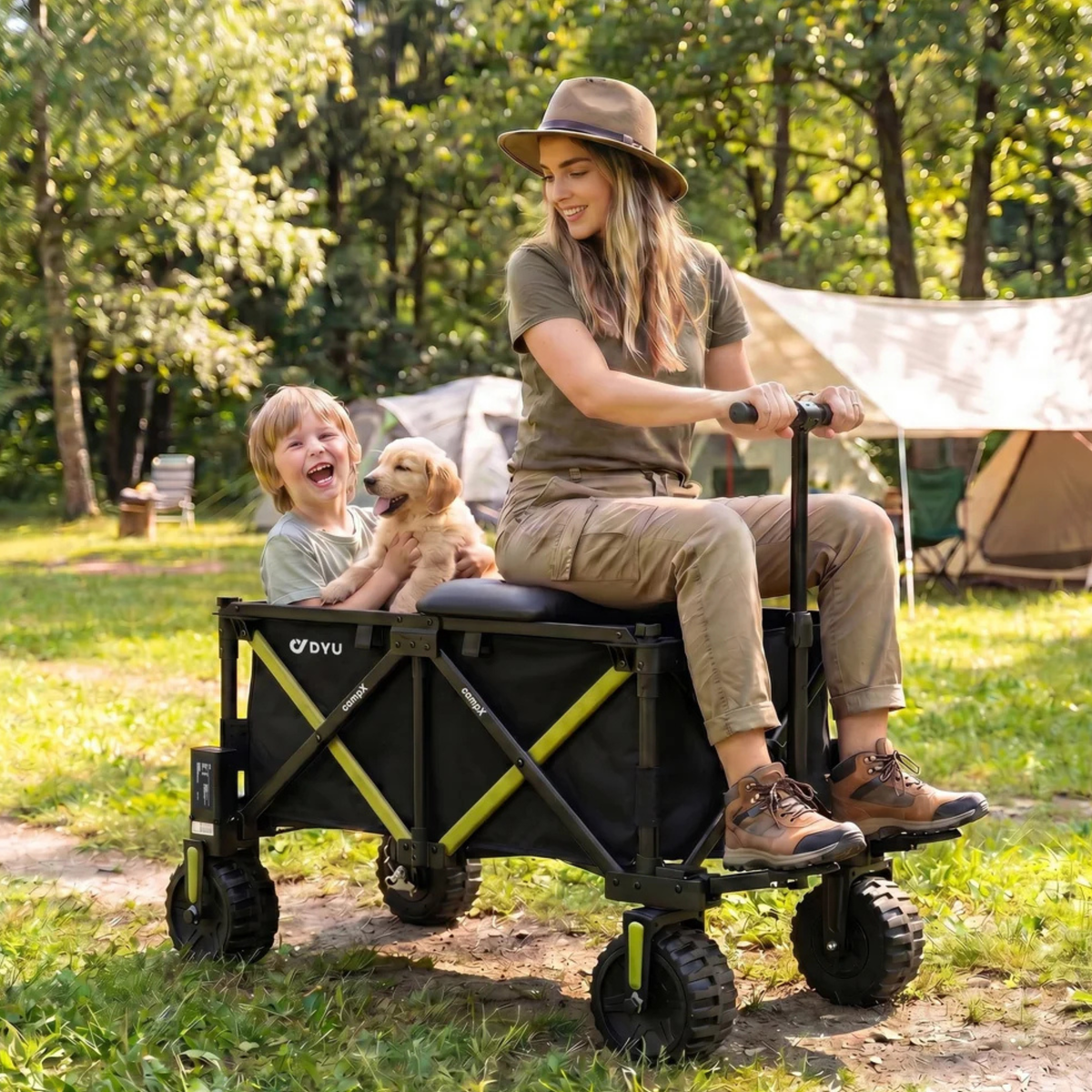 DYU CampX on grass by a tent, a woman sitting on the wagon and a child with a puppy inside it