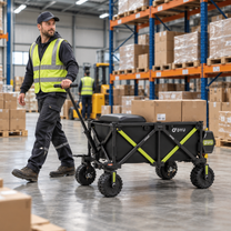 Black DYU CampX wagon with green details and boxes on top, pulled by a man in a hi-vis vest in a warehouse
