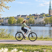 Woman wearing a helmet riding a white OneSport OT12 Pro along the water with a city in the background