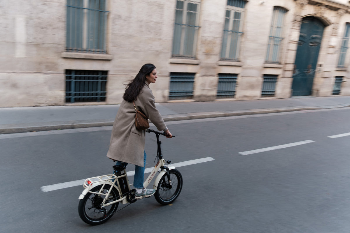 OneSport OT16 Pro: woman in a coat riding on a street in front of a stone facade, side view