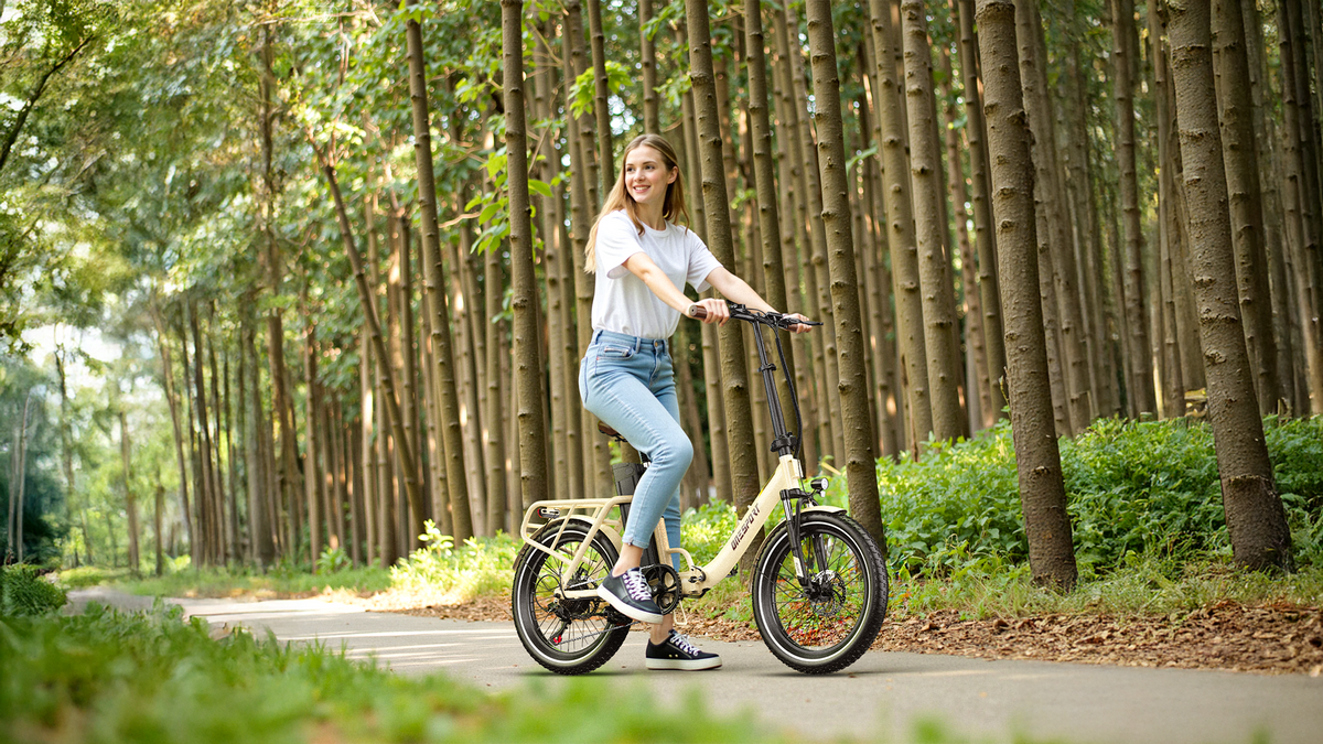 Smiling woman standing with a cream-white OneSport OT16 Pro on a forest path among tall tree trunks