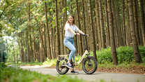 Smiling woman standing with a cream-white OneSport OT16 Pro on a forest path among tall tree trunks