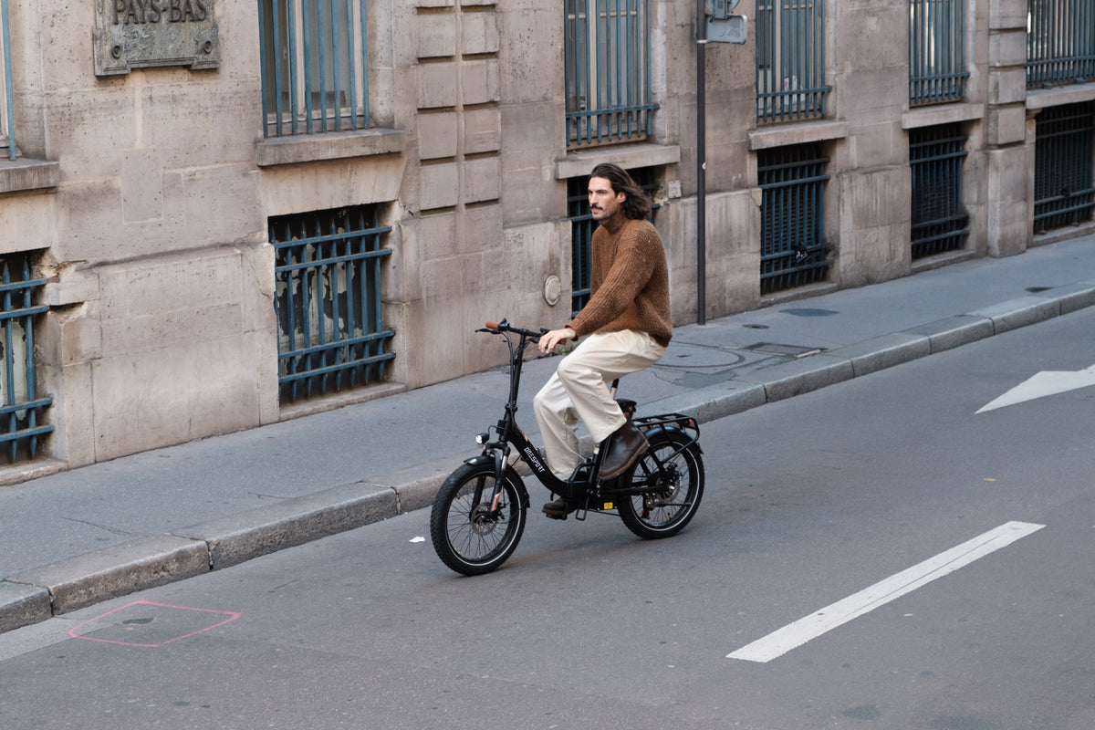Man riding the OneSport OT16 Pro, a black bike, on a street along a stone building with barred windows