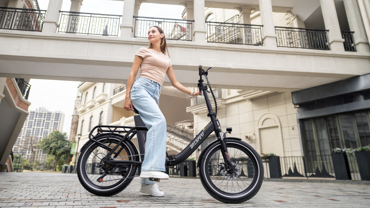 OneSport OT16 Pro: black bike in side view with a woman standing beside it on a paved area