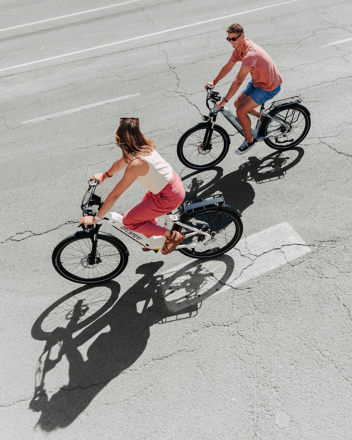 OneSport WT05 seen from above, a woman on a white bike and a man on a grey bike riding on asphalt with shadows