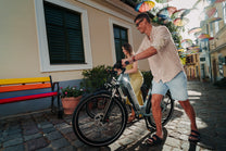 OneSport WT05 in side view, a man holding the handlebars while a woman stands behind with a bike on a street with umbrellas