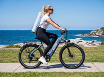 OneSport WT05 in side view, a woman with a yoga mat on her back riding along the sea