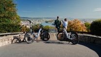 Two OneSport WT05 bikes parked by a stone railing at a viewpoint with two people and a view over the city and river