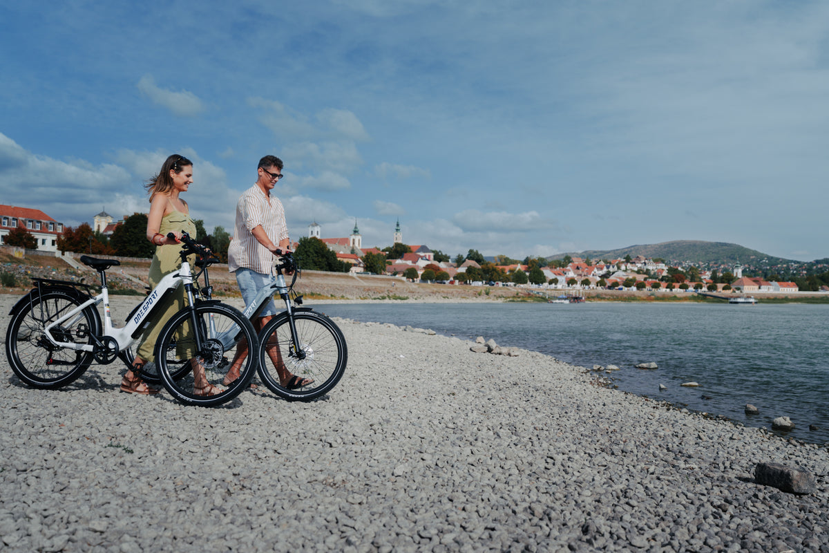 Two people each walking a OneSport WT05 along a stony beach with a city and hill in the background