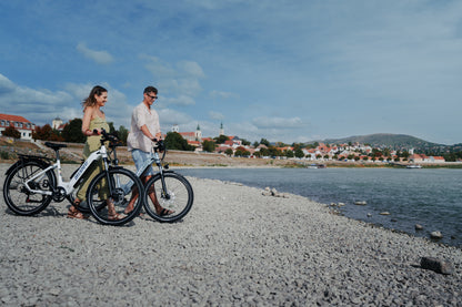 Two people each walking a OneSport WT05 along a stony beach with a city and hill in the background