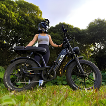 Woman riding the TST R7 fat-tyre e-bike in black on a grassy field