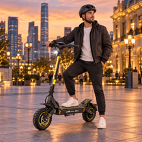 Man wearing a helmet standing with one foot on a black and yellow electric scooter in a square at dusk