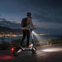 Person wearing a helmet and backpack riding Wheely - J18 on a coastal road at dusk with the headlight on