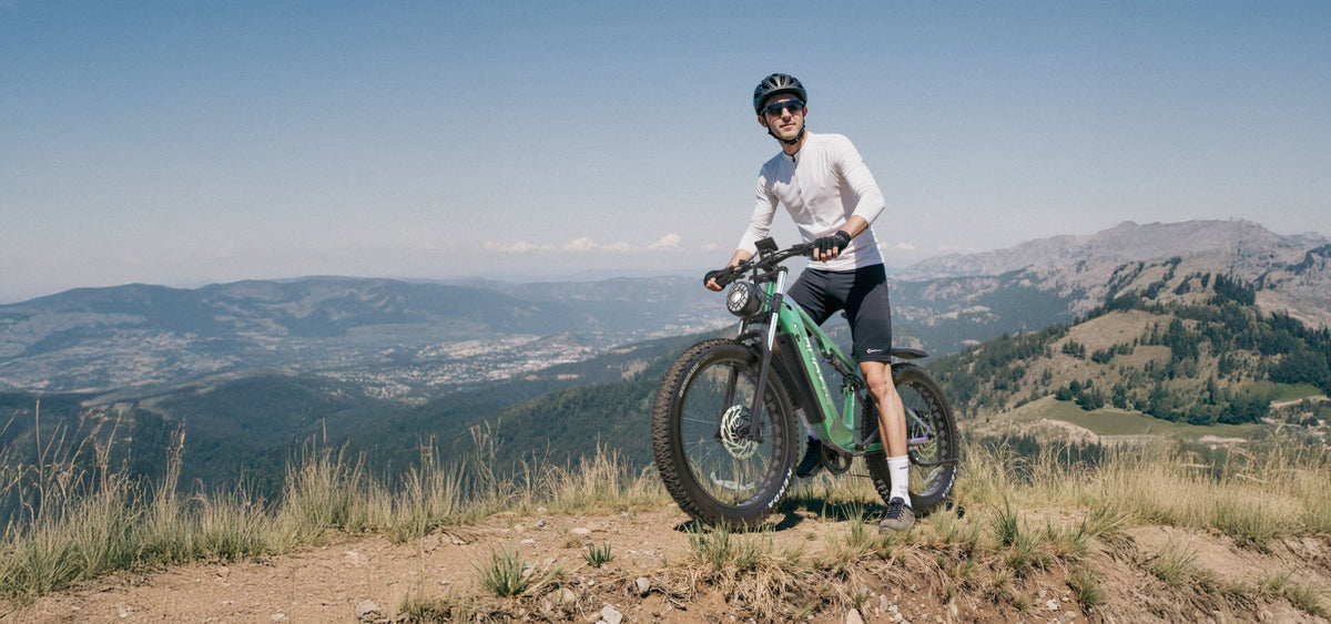 Man standing with the Duotts E26 fat-tyre e-bike on a grassy field in the mountains
