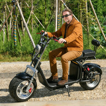 Man sitting on the eHoodax X10 City Road electric scooter on a gravel road