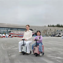 Two people each riding a PowerDrive Pro Edition electric ride-on suitcase outdoors