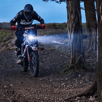 KuKirin X1 electric dirt bike with lights on in an evening setting