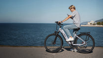 Person riding the OneSport OT05 Pro e-bike wearing a helmet by the sea in light blue