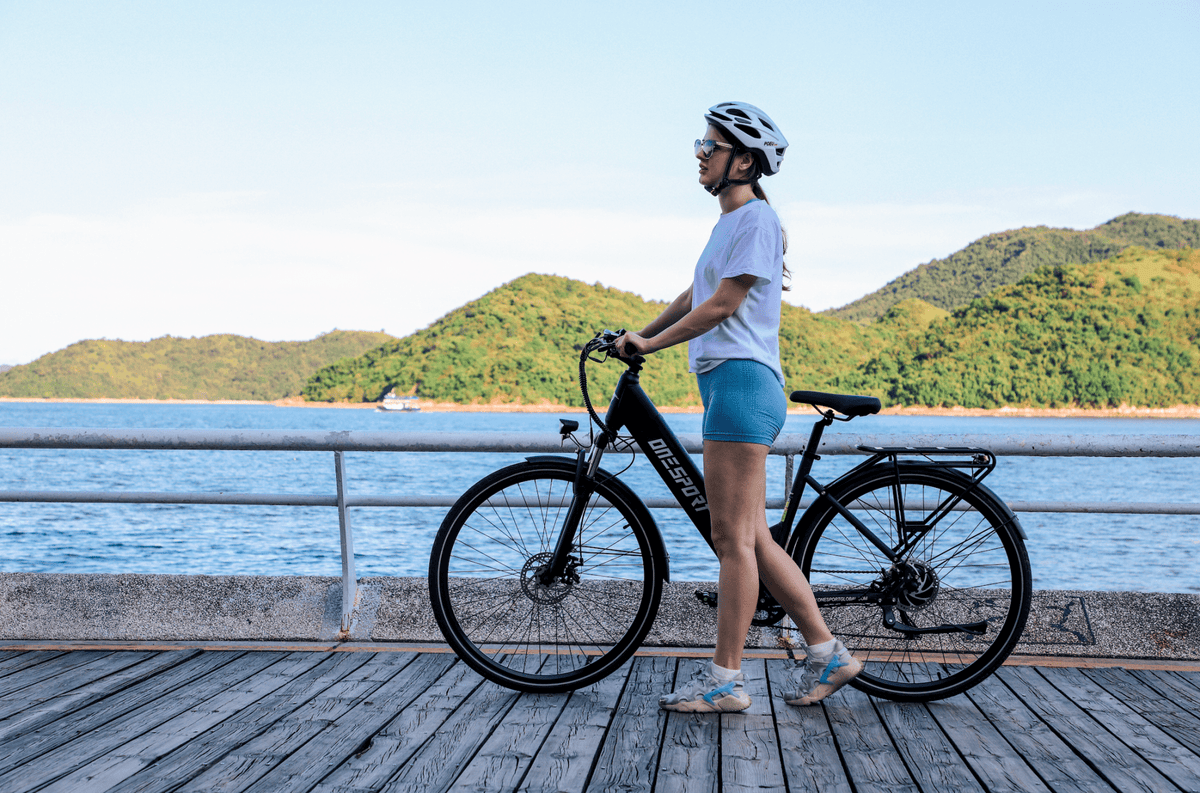 Woman standing with the OneSport OT12 e-bike in black by the sea