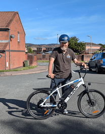Man standing with the VARUN M24-1 electric mountain bike in white wearing a helmet on a street